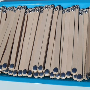 May include: A tray of light brown leather wristbands with silver metal snaps. The wristbands are arranged in rows and are all the same size.