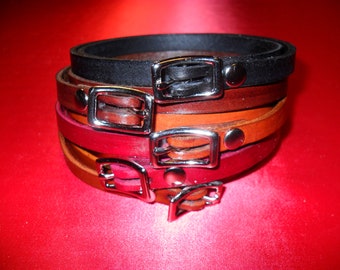 Puede incluir: Un conjunto de cuatro pulseras de cuero con hebillas plateadas. Las pulseras son en tonos marrones y negros.