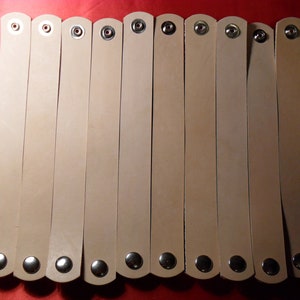 May include: Twelve beige leather bracelets with silver snap closures.