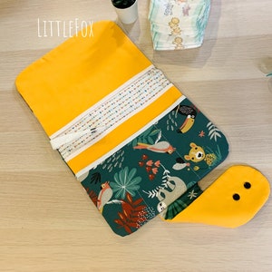 May include: A yellow and green fabric changing mat with a jungle animal print. The mat has a flap that folds over to create a pocket. The mat is labelled "Little Fox".