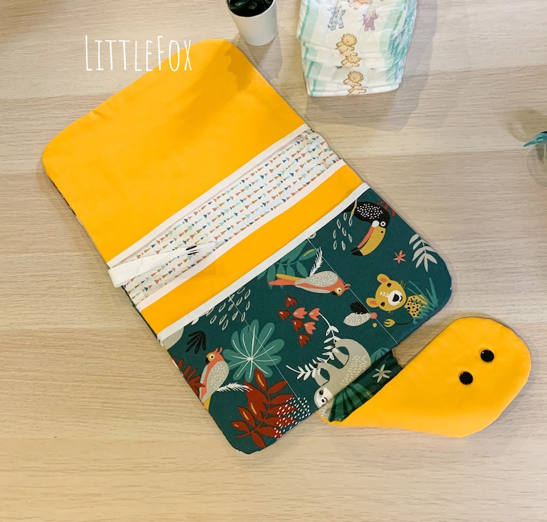 May include: A yellow and green fabric changing mat with a jungle animal print. The mat has a flap that folds over to create a pocket. The mat is labelled "Little Fox".