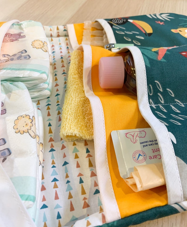 May include: A green and yellow fabric organiser with multiple pockets. The pockets contain baby wipes, a yellow washcloth, a pink bottle with a cap, and a tube of baby cream. The cream tube has the text "Gentle Care and Protection from the causes".