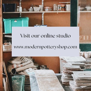 May include: A pottery studio with shelves stocked with supplies, a table with stacks of ceramic tiles, and a pair of green rubber boots. The text on the sign reads "Visit our online studio www.modernpotteryshop.com".