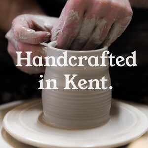 May include: A potter's hands shaping a white ceramic mug on a pottery wheel. The text "Handcrafted in Kent" is displayed in white, emphasizing the handmade nature and location of the craft.