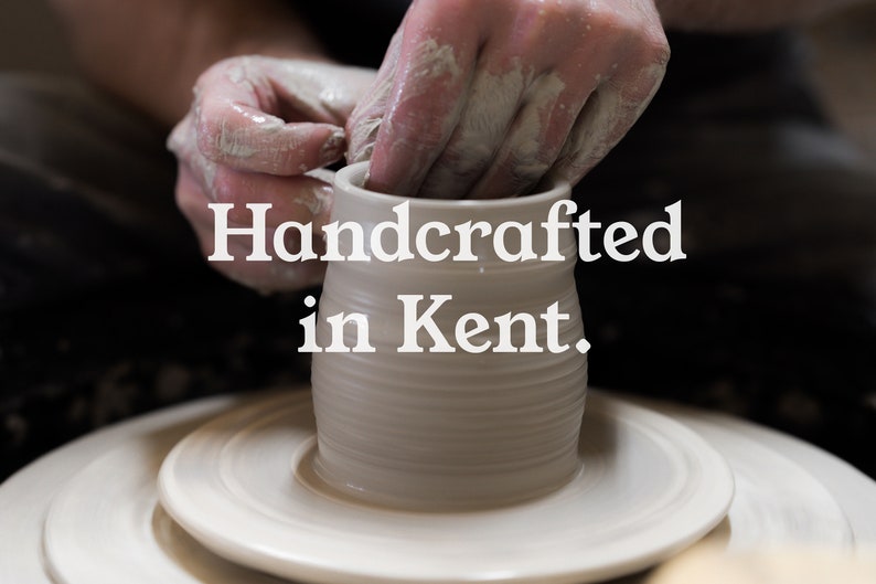 May include: A potter's hands shaping a white ceramic mug on a pottery wheel. The text "Handcrafted in Kent" is displayed in white, emphasizing the handmade nature and location of the craft.