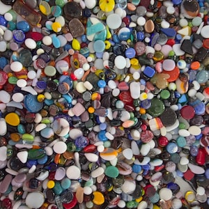 May include: A large collection of small, smooth glass pieces in a wide variety of shapes, sizes, and colors including red, blue, yellow, green, white, black, and clear. The pieces have varying textures, some opaque and some translucent.