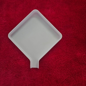 May include: A white diamond-shaped plastic tray with a small pouring spout at the bottom corner. The tray features raised edges to contain small items and is designed for sorting or transferring beads, diamonds, or other small craft components.