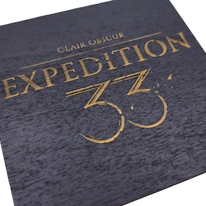Puede incluir: Un cuadrado azul oscuro texturizado con esquinas redondeadas. Las palabras "CLAIR OBSCUR" están en la parte superior, con "EXPEDITION 33" en oro, en relieve. El número "33" se muestra de forma destacada.