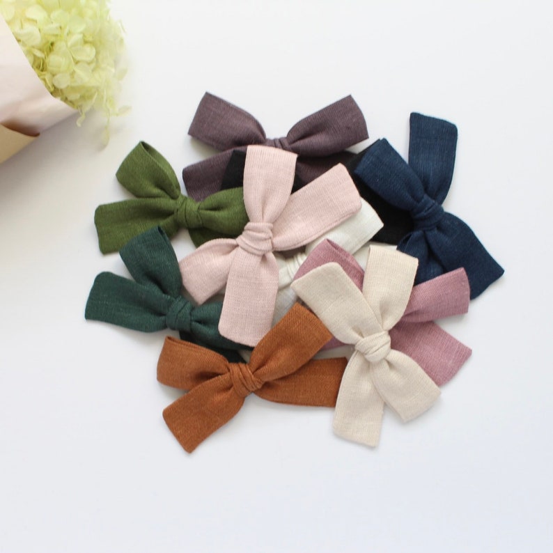 Puede incluir: Un conjunto de diez lazos para el pelo de tela en varios colores, incluyendo verde, marr&oacute;n, rosa, beige y azul. Los lazos est&aacute;n hechos de una tela suave y texturizada y est&aacute;n atados con un simple nudo.