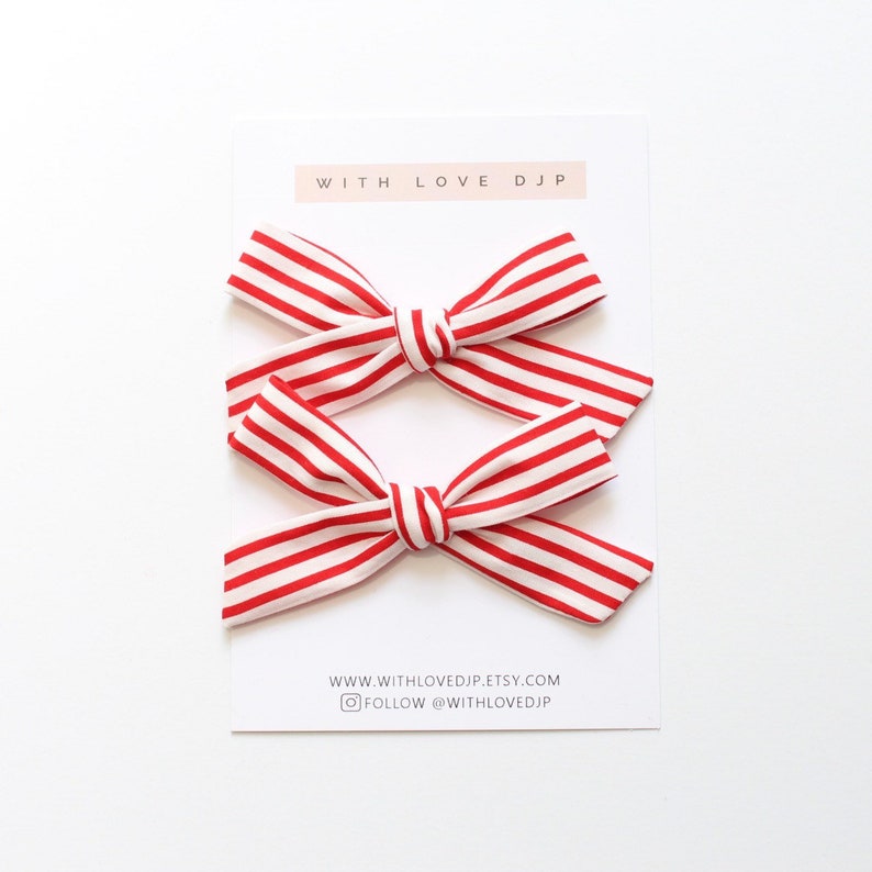 May include: Two red and white striped hair bows. The bows are tied in a knot and are ready to be worn. The bows are on a white background with the text "WITH LOVE DJP" and "WWW.WITHLOVEDJP.ETSY.COM FOLLOW @WITHLOVEDJP".