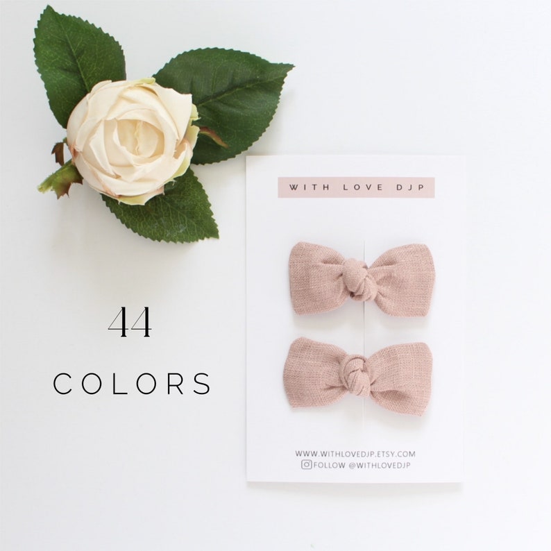 May include: Two dusty rose fabric hair bows with a knotted center. The bows are displayed on a white card with the text "WITH LOVE DJP" and "WWW.WITHLOVEDJP.ETSY.COM" and "FOLLOW @WITHLOVEDJP". The text "44 COLORS" is written below the bows.