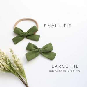 Puede incluir: Dos lazos para el pelo de tela verde, uno en una diadema el&aacute;stica de color nude. El lazo m&aacute;s peque&ntilde;o est&aacute; etiquetado como "SMALL TIE" y el lazo m&aacute;s grande est&aacute; etiquetado como "LARGE TIE (SEPARATE LISTING)"