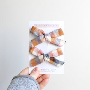 May include: Three plaid hair bows in shades of pink, orange, and blue. The bows are arranged on a white card with the text "WITH LOVE DJP" at the top and "WITHLOVEDJP.ETSY.COM FOLLOW @WITHLOVEDJP" at the bottom.