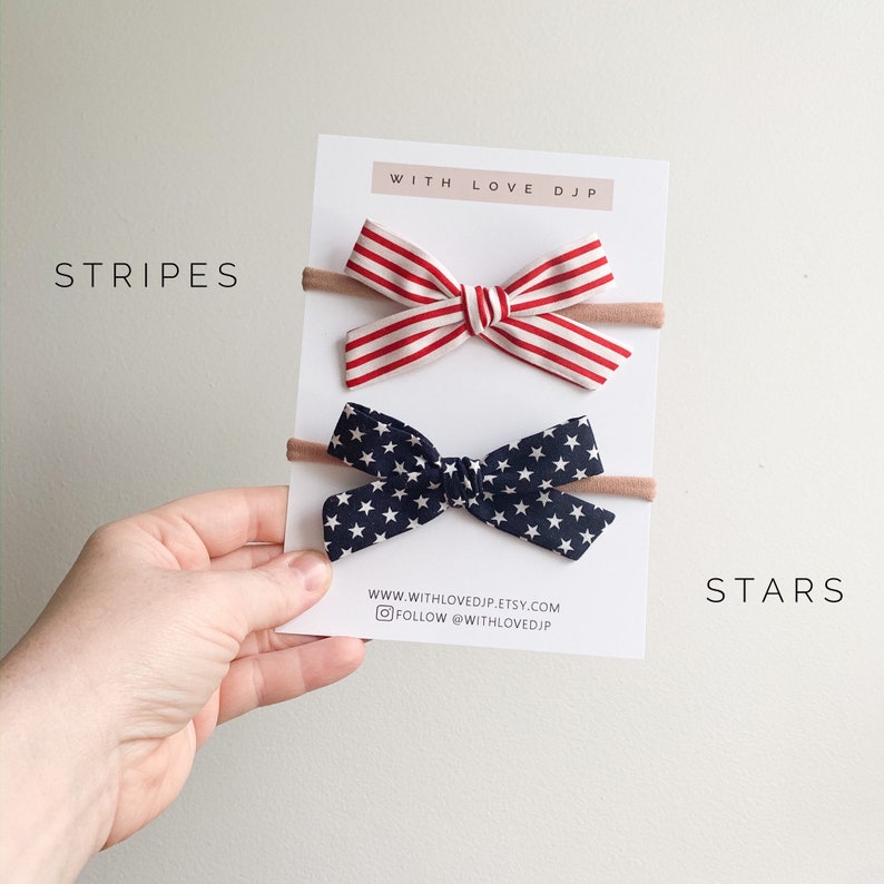 Puede incluir: Dos lazos para el pelo en una tarjeta blanca con el texto "WITH LOVE DJP" y la direcci&oacute;n del sitio web "www.withlovedjp.etsy.com". El lazo de arriba es de rayas rojas y blancas. El lazo de abajo es azul marino con estrellas blancas. El texto "STRIPES" est&aacute; en el lado izquierdo de la tarjeta y "STARS" est&aacute; en el lado derecho de la tarjeta.