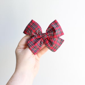 May include: A red and green plaid bow, tied with a knot in the center.