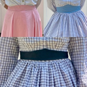 May include: Three different styles of gingham skirts with contrasting fabric belts. The first skirt is pink with a white belt, the second is blue and white gingham with a light blue belt, and the third is gray and white gingham with a black belt.