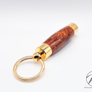 Peut inclure: Un porte-clés doré avec une poignée en bois brun. La poignée présente un motif de grain de bois unique.