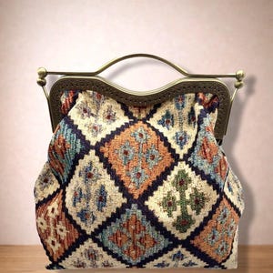 May include: A structured handbag featuring a woven tapestry fabric with a repeating diamond pattern in shades of orange, blue, green, and cream. The bag has a dark bronze-toned metal frame with an arched handle and a decorative embossed edge.