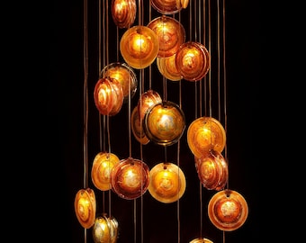Op de afbeelding: Een moderne kroonluchter met meerdere ronde, amberkleurige glazen lampenkappen die aan een zwart plafond hangen. De lampenkappen zijn van verschillende grootte en hebben een draaiend patroon.