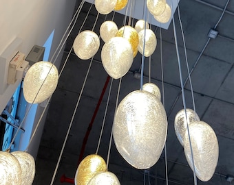 Op de afbeelding: Een moderne kroonluchter met meerdere heldere glazen bolvormige armaturen die aan een plafond hangen. De bollen zijn getextureerd en hebben een mat uiterlijk. De kroonluchter hangt aan een ronde metalen plaat.