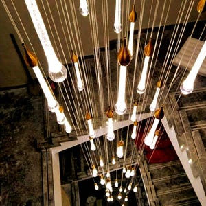 Long 4-story cascading Ferraro Chandelier in Clear glass with Silver particles by staircase. High Ceiling Design Idea