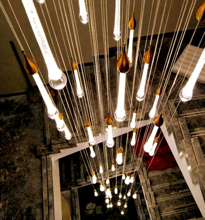 Long 4-story cascading Ferraro Chandelier in Clear glass with Silver particles by staircase. High Ceiling Design Idea