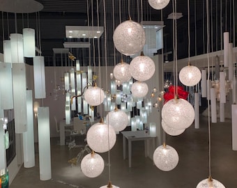 Op de afbeelding: Een verzameling bolvormige glazen hanglampen met een textuur van barstjes, opgehangen op verschillende hoogtes aan het plafond. Elke bol bevat een interne lichtbron die een warme gloed door het doorschijnende glas verspreidt.