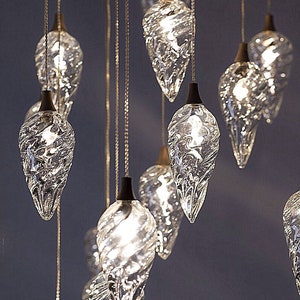 May include: A chandelier with multiple teardrop-shaped glass bulbs hanging from a ceiling. The bulbs are clear and have a textured surface. The bulbs are lit and emit a warm glow.