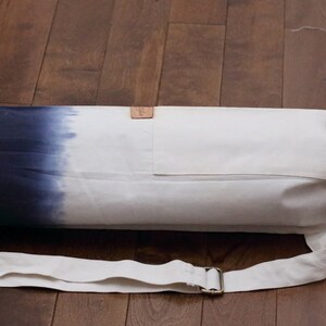 May include: A white and blue ombre yoga mat bag with a drawstring closure and an adjustable shoulder strap. The bag has a small pocket on the front.
