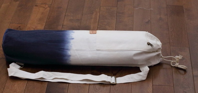 May include: A white and blue ombre yoga mat bag with a drawstring closure and an adjustable shoulder strap. The bag has a small pocket on the front.
