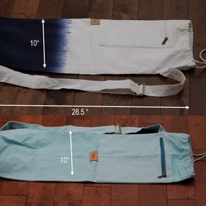 May include: Two yoga mat bags, one with a blue and white ombre design and the other a light blue color. Both bags have a zippered pocket and a drawstring closure. The bags measure 10 inches wide and 28.5 inches long.