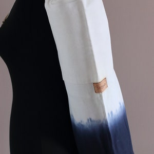 May include: White canvas yoga mat bag with a drawstring closure and a zippered pocket. The bag has a blue ombre design and a brown leather label that says "Remarkable".