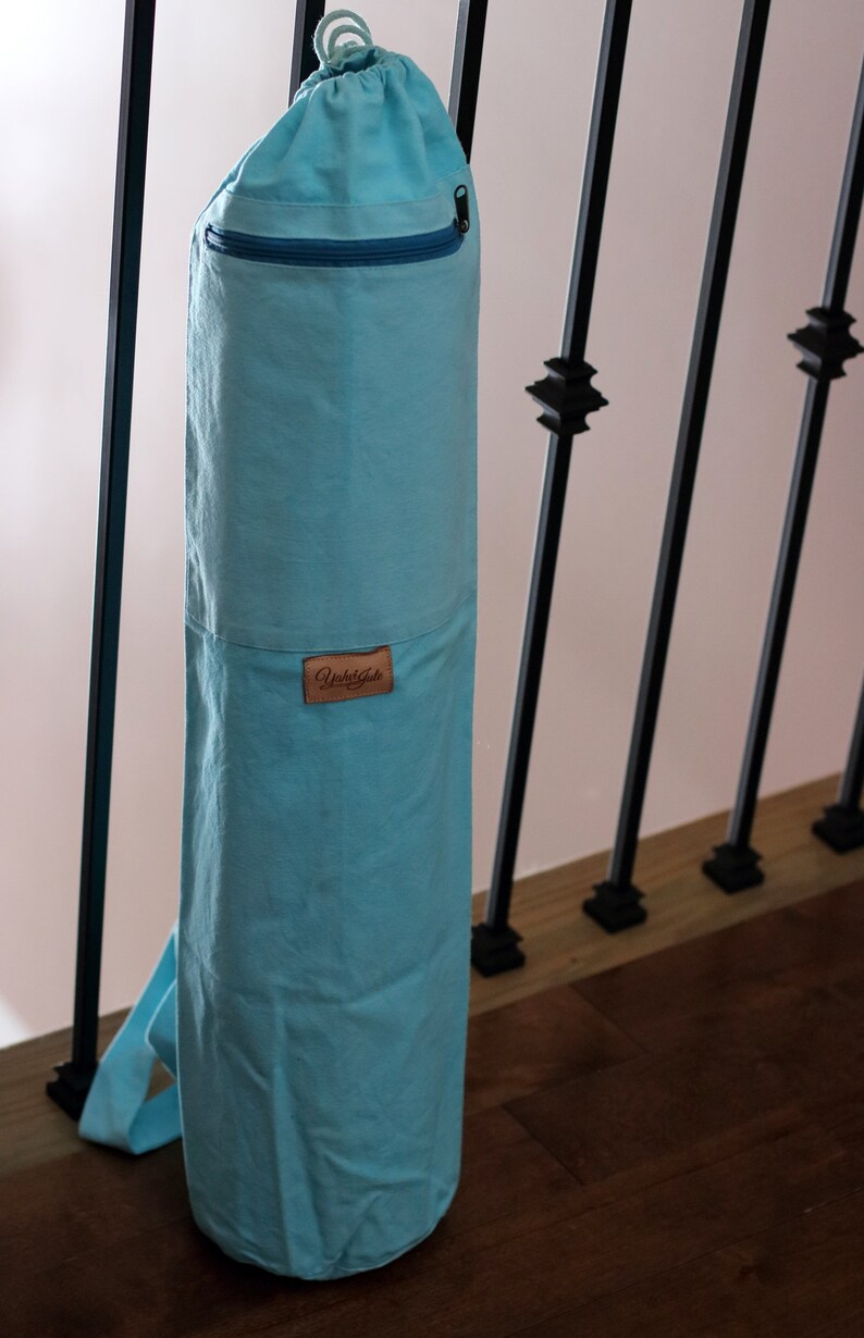 May include: A light blue yoga mat bag with a zippered pocket and a brown leather label that says "Yuka Gate".
