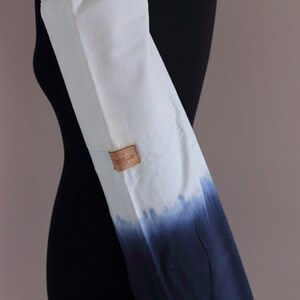May include: White canvas yoga mat bag with a blue ombre dye pattern. The bag has a zippered pocket and a leather label that says "Studio Kate".