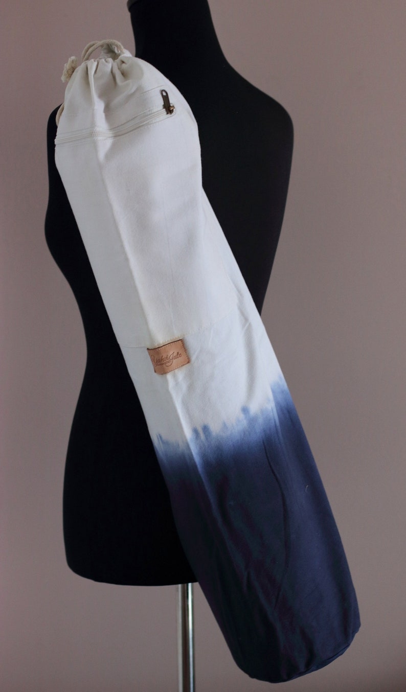 May include: White canvas yoga mat bag with a blue ombre dye pattern. The bag has a zippered pocket and a leather label that says "Studio Kate".