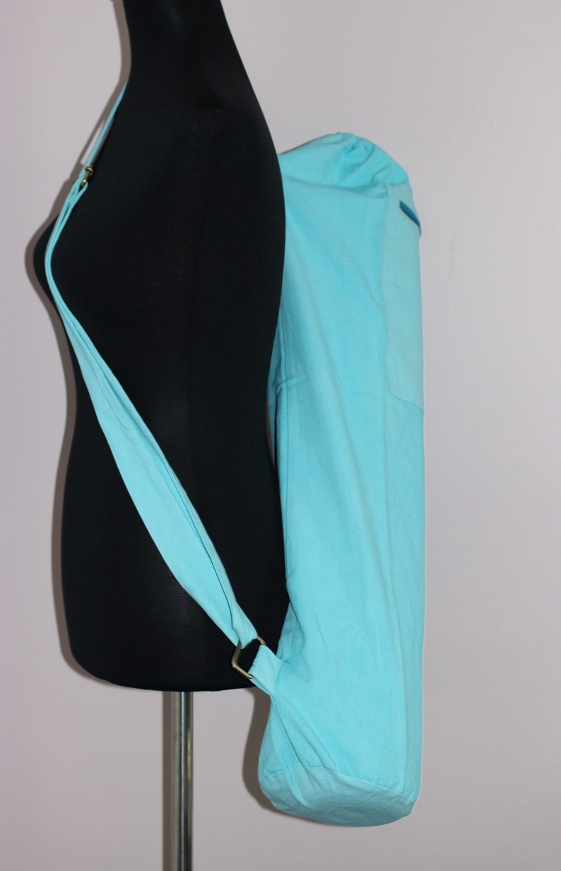 May include: A light blue yoga mat bag with a long strap. The bag is made of fabric and has a drawstring closure.