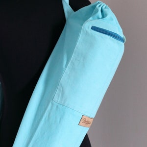 May include: A light blue yoga mat carrier with a zippered pocket and a brown leather label that says "Yubba"