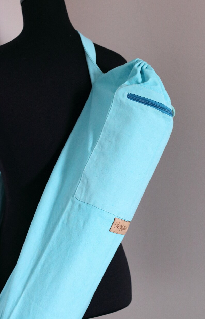 May include: A light blue yoga mat carrier with a zippered pocket and a brown leather label that says "Yubba"