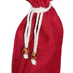May include: A red burlap drawstring bag with white cords and wooden beads. The bag is lined with a gold fabric.
