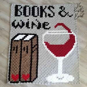 Peut inclure: Une couverture en crochet gris avec les mots "BOOKS & WINE" en fil noir. Une pile de livres et un verre de vin rouge sont crochetés dans la couverture.