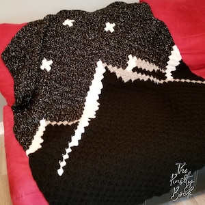 Peut inclure: Une couverture en crochet noir et blanc avec un motif de montagne et d'étoiles. La couverture est faite avec un fil scintillant et a un motif texturé.