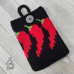 Könnte beinhalten: Schwarze gehäkelte Handyhülle mit einem roten und grünen Chili-Pfeffer-Design. Die Hülle hat einen Knopfverschluss und eine Schlaufe zum Aufhängen.