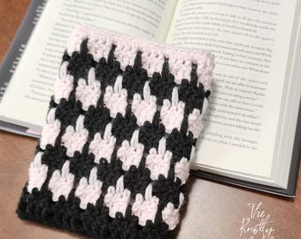 Puede incluir: Un marcapáginas de crochet negro y rosa en forma de dedo corazón.