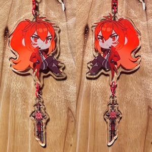 May include: Two clear acrylic keychains featuring a chibi-style character with red hair and a red outfit. Each keychain has a red sword charm hanging below. The character is sitting with a stern expression. The keychains are attached with red cords.