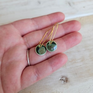 May include: A pair of green and black ceramic earrings with gold hoops. The earrings are round and have a speckled pattern.