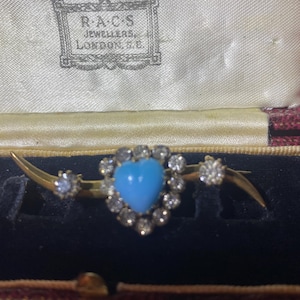 May include: A heart-shaped turquoise brooch with a diamond halo, set in gold. The brooch is in a black velvet box with a label that reads "R.A.C.S. Jewellers, London, W.C."