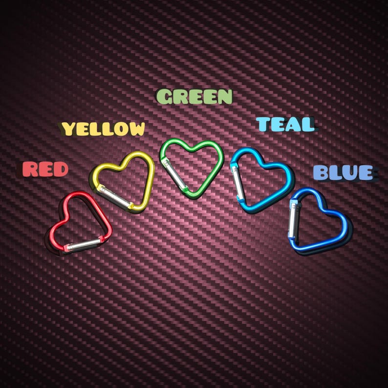 May include: Five heart-shaped carabiners in red, yellow, green, teal, and blue, each featuring a spring-loaded gate. The text labels RED, YELLOW, GREEN, TEAL, and BLUE are positioned above their respective colored carabiners on a dark background.