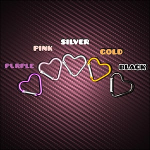 May include: Five heart-shaped carabiners arranged in a row, each featuring a different metallic finish. The colors are labeled as PURPLE, PINK, SILVER, GOLD, and BLACK. Each carabiner includes a spring-loaded gate mechanism for secure attachment.
