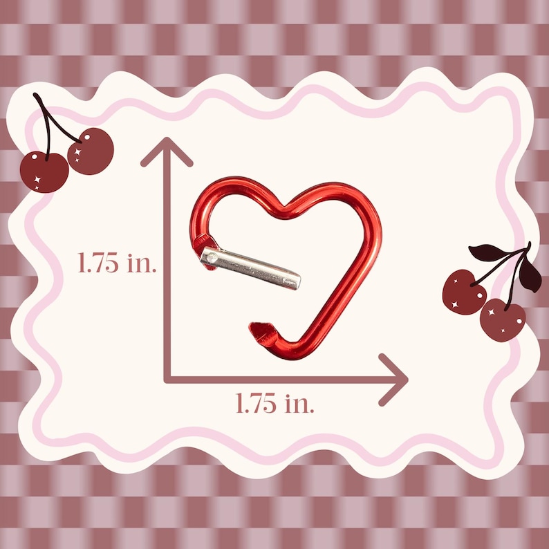 May include: A red heart-shaped carabiner with a silver-toned spring gate. The carabiner is displayed with measurement lines indicating a height and width of 1.75 inches. The design features a smooth, metallic finish and a functional opening mechanism.