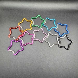 Puede incluir: Una colecci&oacute;n de diez mosquetones con forma de estrella en varios colores, incluyendo rojo, naranja, verde, azul claro, azul oscuro, rosa, morado, plateado y negro. Cada mosquet&oacute;n de metal cuenta con un mecanismo de cierre de resorte.